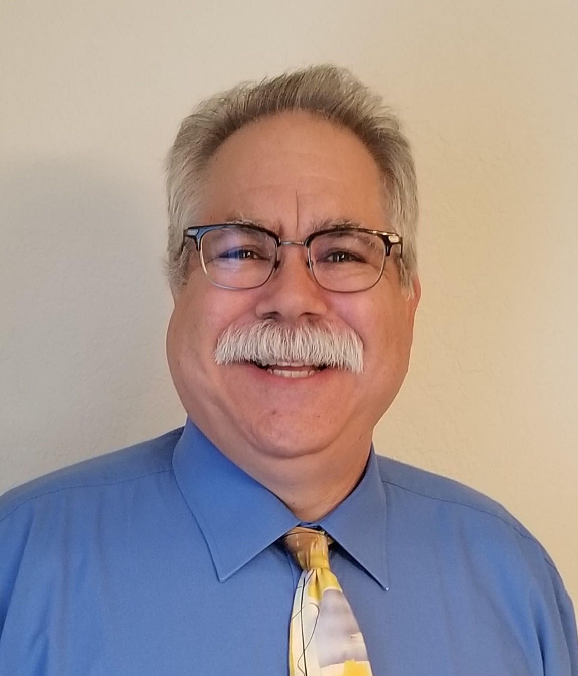 Smiling person with mustache, glasses, blue shirt, tie