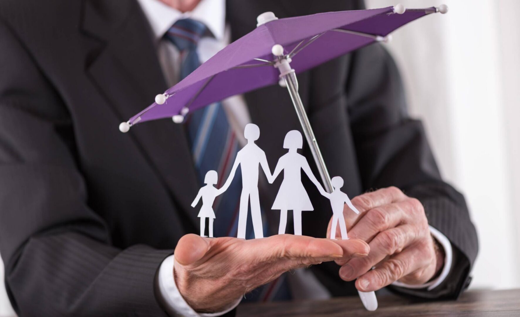 Businessman shielding paper family with purple umbrella