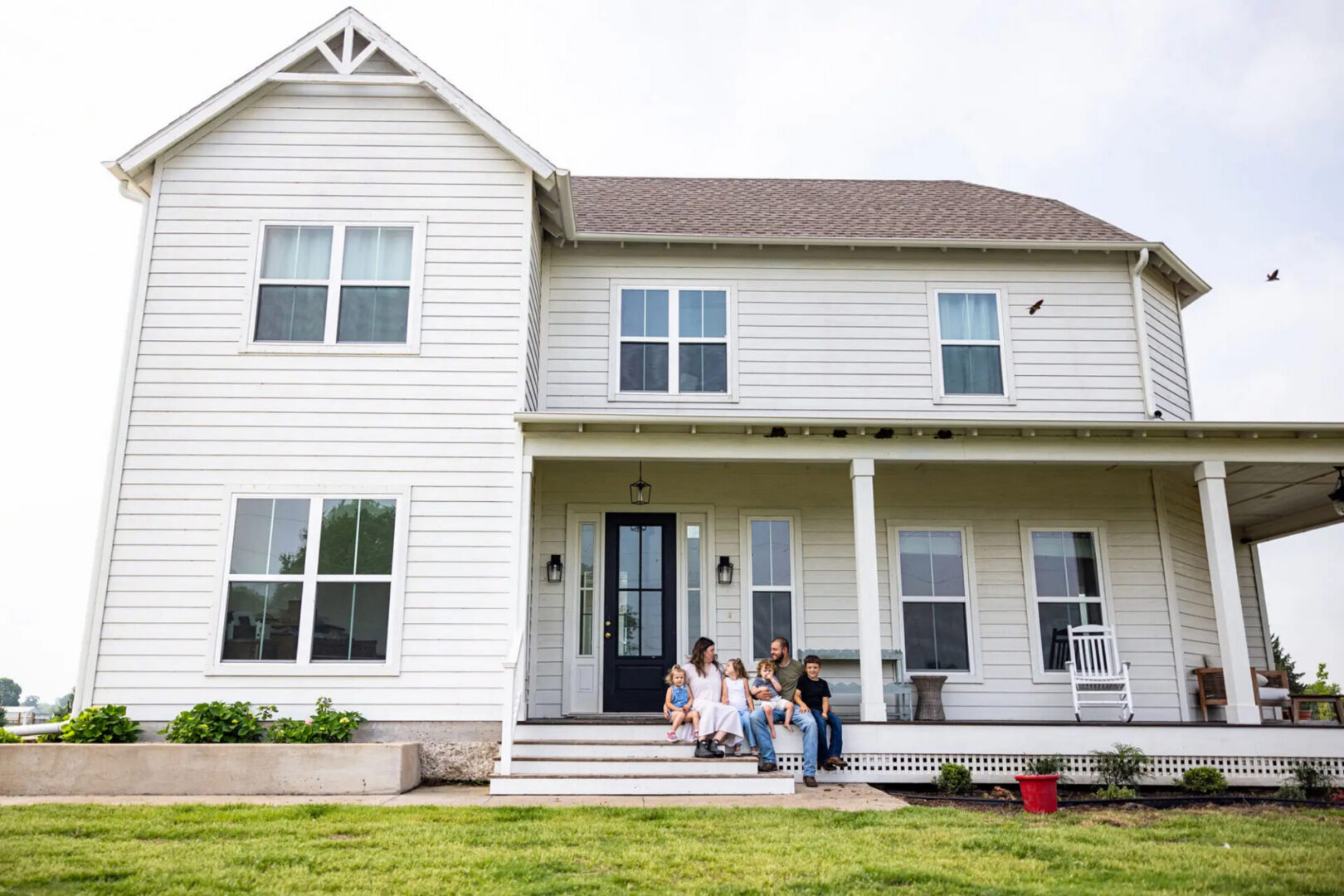 Family sitting on porch of white farmhouse