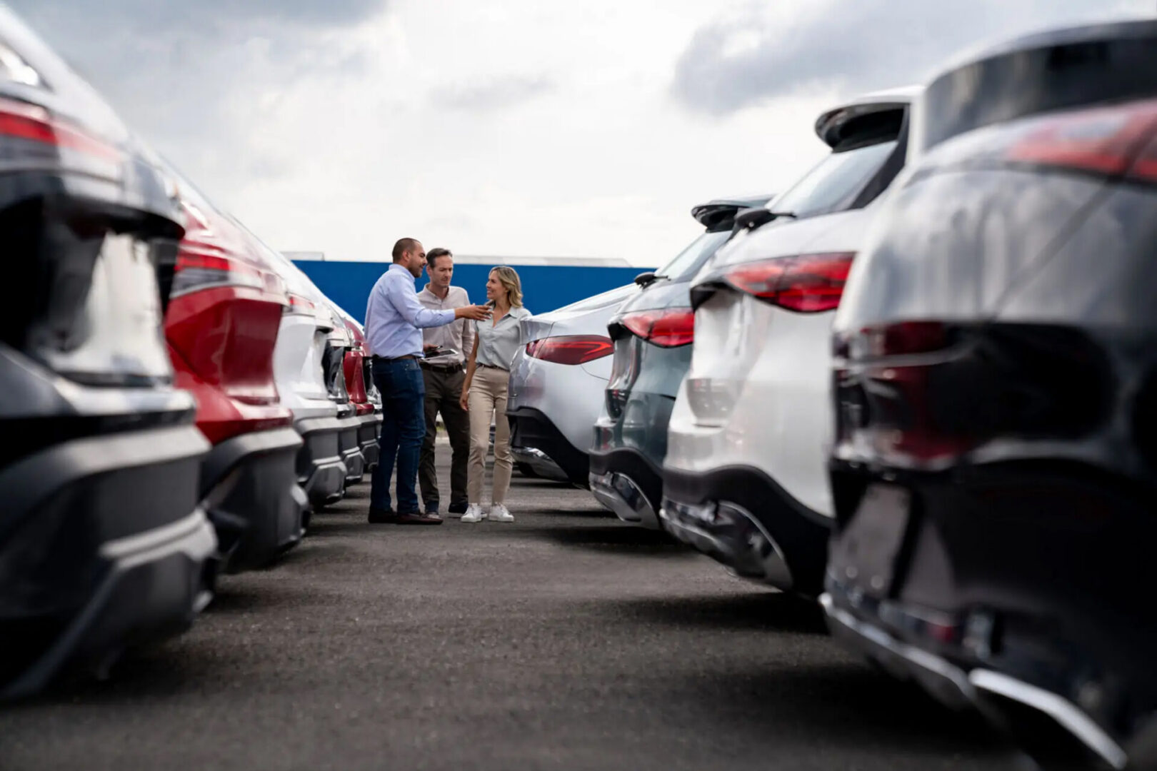 Three people inspecting cars in dealership lot